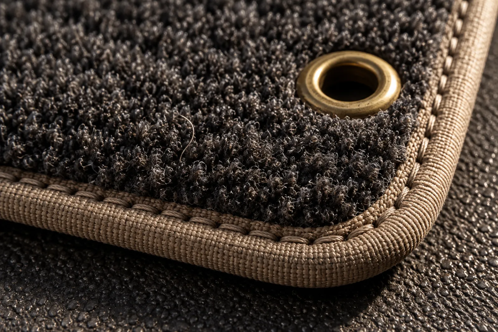 Detalle de esquina de alfombrilla velour con ribete beige y ojal metálico