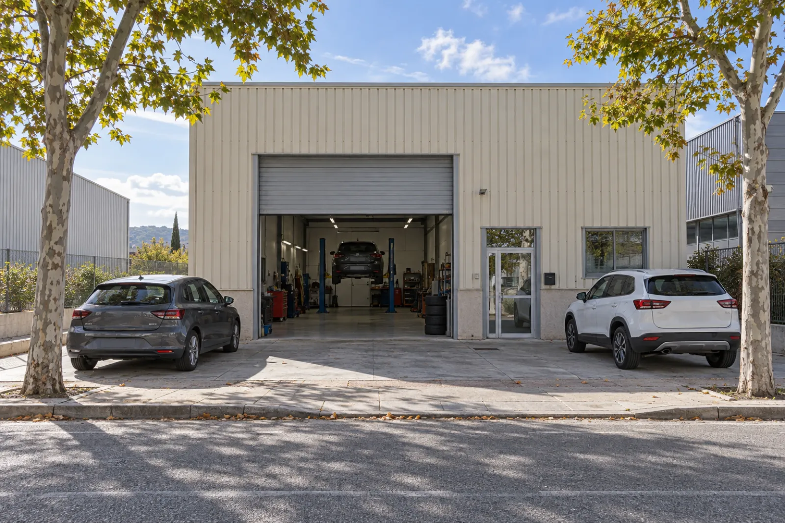Fachada de la nave del taller en Coslada con la puerta abierta y dos coches aparcados